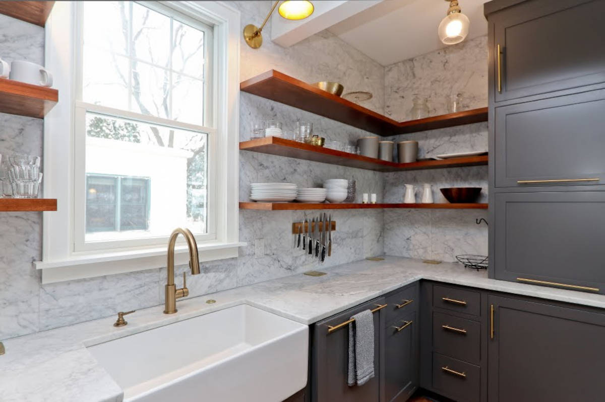 Kitchen with dark grey cabinets, red wood floating shelves, and farmhouse sink. Gold hardware.
