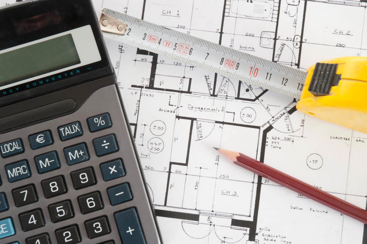 Blueprint with tape measurer, calculator, and pencil laying over it.